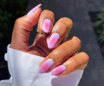 Hand with aura nails, smooth gradient of pink and purple hues, white cuff visible in sunlight.