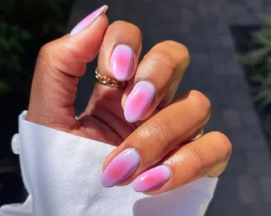 Hand with aura nails, smooth gradient of pink and purple hues, white cuff visible in sunlight.