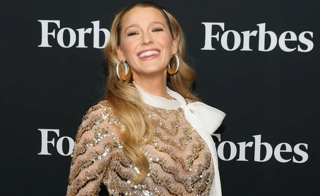 Smiling woman in a sparkling dress with large earrings at a Forbes event.