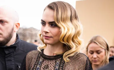 A woman with wavy blonde hair in a black netted top, surrounded by people outdoors.