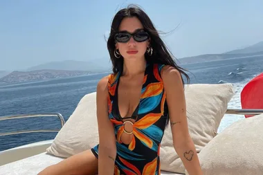 Woman in a colorful swimsuit sitting on a yacht deck, with ocean and distant hills in the background.