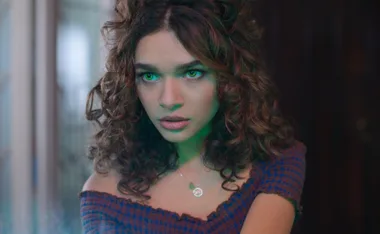 A young woman with curly hair and glowing green eyes, looking intense, from Fate: The Winx Saga.