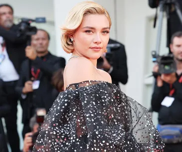 Person in shimmering black gown poses on Venice Film Festival red carpet, surrounded by photographers.