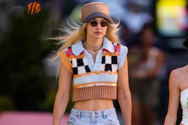 Person wearing a colorful crochet top, sunglasses, and a hat, walking outdoors.