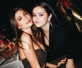 Two women posing closely at a dimly lit event with candles and floral decor in the background.