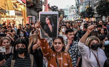 Protesters in a crowd hold a portrait of a woman during a demonstration on a city street.