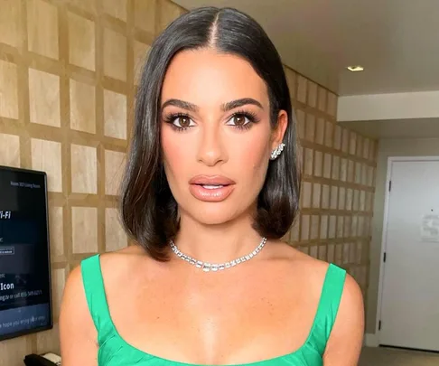 A woman in a green dress with a diamond necklace and earrings, posing indoors with a neutral expression.