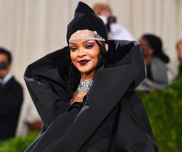 Rihanna at a red carpet event wearing an elaborate black outfit and jeweled headpiece, smiling confidently.