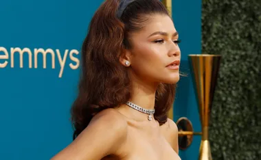 Zendaya poses at the 2022 Emmys in an elegant dress, with a blue background featuring the Emmys logo.