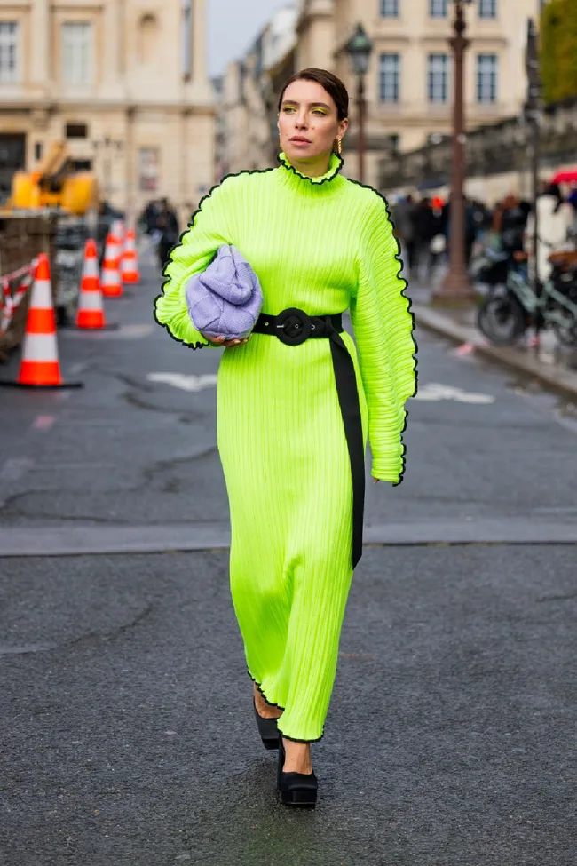 Person in a bright neon green dress walking on a city street, holding a lavender handbag.