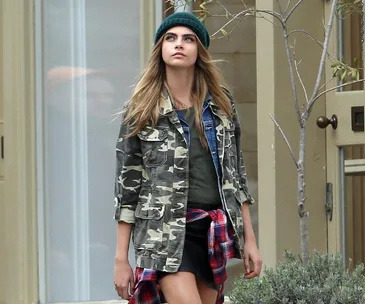 Woman in camouflage jacket and beanie walking outside.