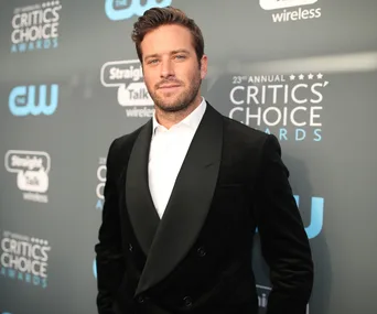 Man in a black suit at Critics' Choice Awards red carpet event, standing against a branded backdrop.