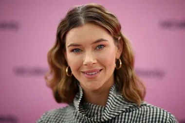 Woman in a checkered top smiling against a pink background.