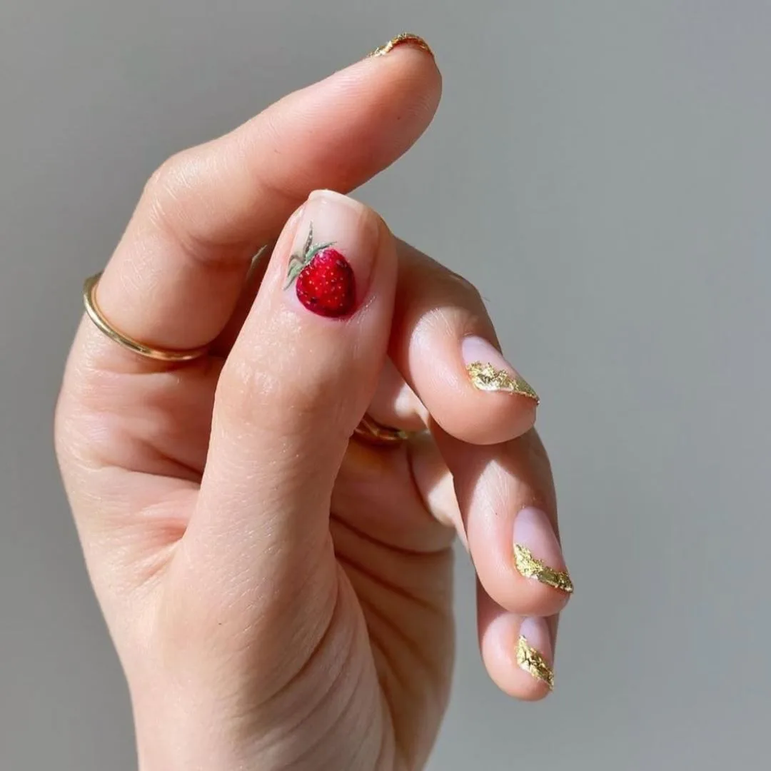 Strawberry thumbnail with sparkling gold tipped nails on rest of hand