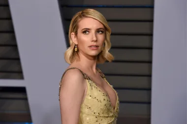 A woman in a yellow embellished gown with short blonde hair and dangling earrings, looking to the side.