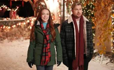 Lindsay Lohan with co-star in a festive, snow-covered setting adorned with Christmas lights.