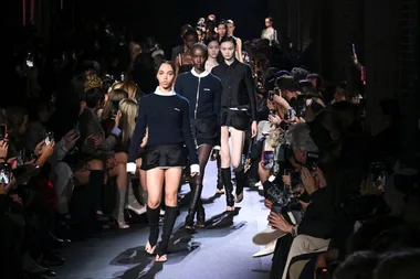 Models walk the runway in black and white outfits during Paris Fashion Week SS23 as audience captures photos.