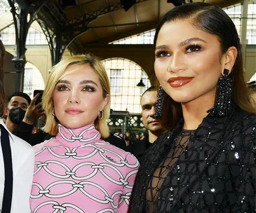 Zendaya and Florence Pugh in elegant, sheer Valentino outfits at a fashion event, standing under an ornate roof structure.