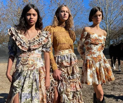 Three models in floral and lace dresses stand outdoors under clear blue sky.