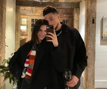 A couple takes a cozy mirror selfie in a warmly decorated wooden room, the man holding a glass of wine.