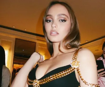 A woman in a stylish black and gold chain dress poses indoors with a confident expression.