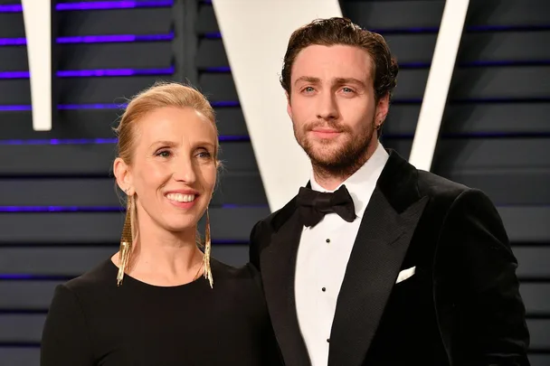 A couple poses together on a red carpet, dressed in formal evening attire and smiling.