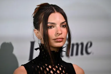 Person in a black dress at an event, neutral expression, blurred background.