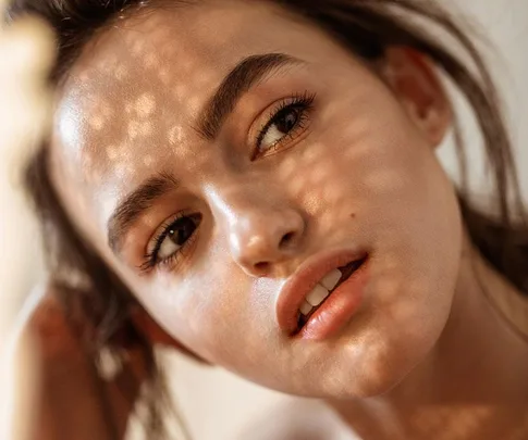 Close-up of a woman's face with sunlight casting patterns, highlighting her skin texture and facial features.