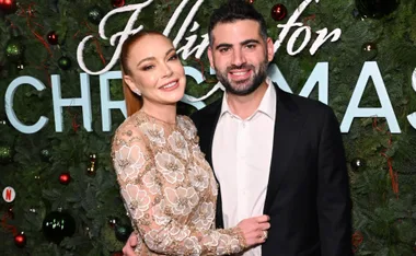 A woman in a floral dress and a man in a suit pose in front of a Christmas-themed backdrop.