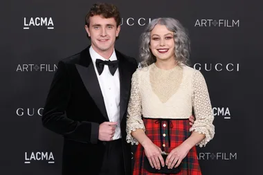 Paul Mescal in a tuxedo and Phoebe Bridgers in a lace top and plaid skirt, smiling at a formal event.