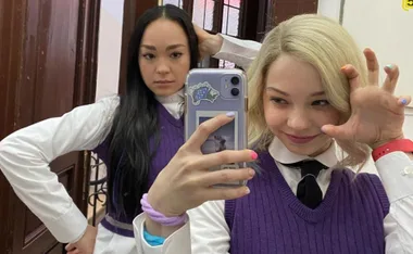 Two young women in purple vests take a mirror selfie, one with a playful claw gesture.