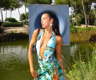 Woman in a vibrant, tropical print summer dress posing near a lake with trees and a blue backdrop.