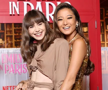 Two women smiling at the "Emily in Paris" Season 3 premiere in front of a themed backdrop.