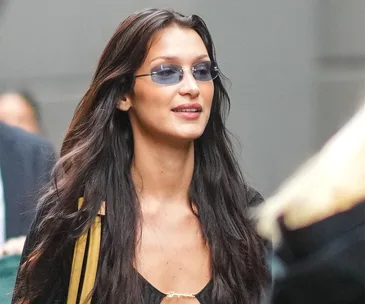 Young woman with long hair wearing small, rimless sunglasses on a busy street.