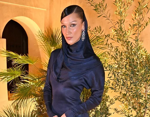 Woman in elegant navy hooded dress with silver earrings stands beside greenery against an arched background.