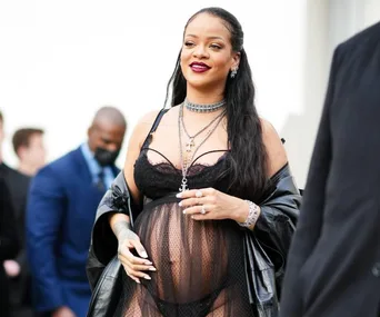 A stylish woman in a sheer black outfit and leather jacket, accessorized with layered necklaces.