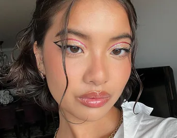 A person wearing glossy lipstick and glittery pink eyeshadow with bold eyeliner and wet hair style.