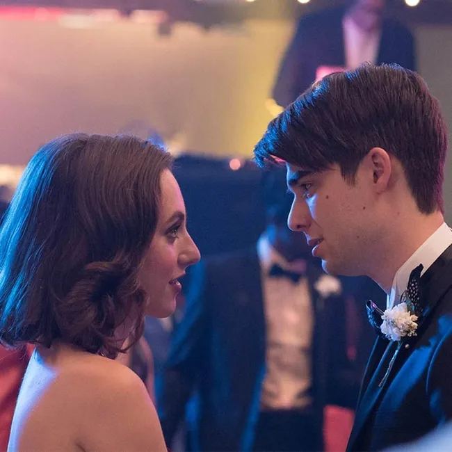 A young couple in formal attire shares a romantic moment on a decorated dance floor with a DJ in the background.
