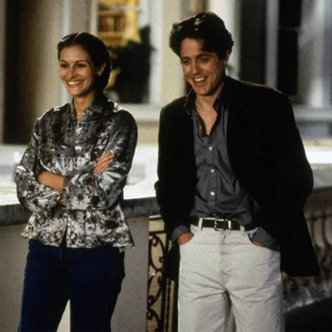 A woman and man stand casually on a balcony, smiling and dressed in casual attire, from the movie "Notting Hill".