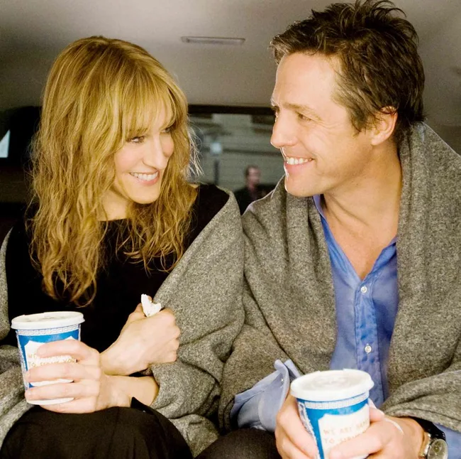 Two people smiling at each other in a car, wrapped in gray blankets, holding cups with lids.