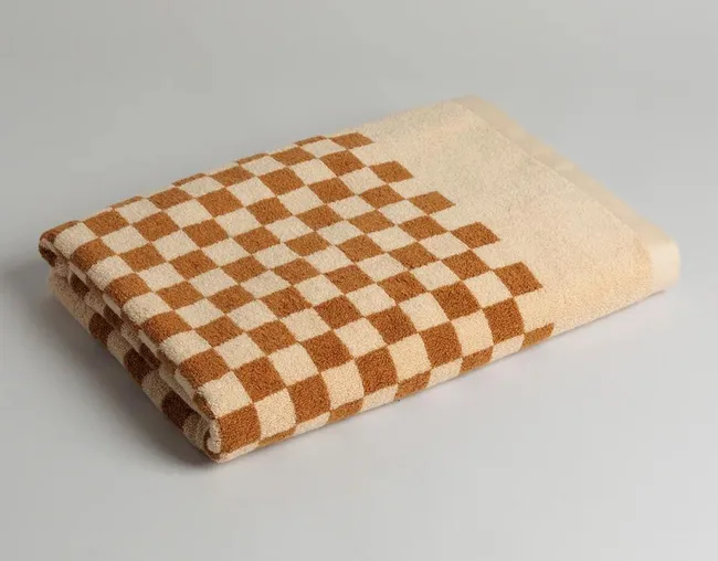 Folded checkered towel with brown and beige squares on a light gray background.