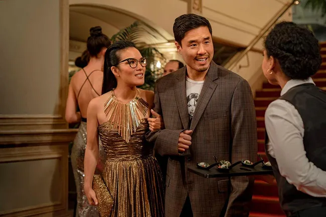 Two people in formal attire smiling, talking to a waiter carrying appetizers in a luxurious setting.