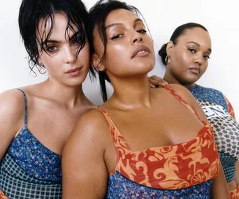 Three women pose confidently in patterned dresses, showcasing diverse styles and attitudes.