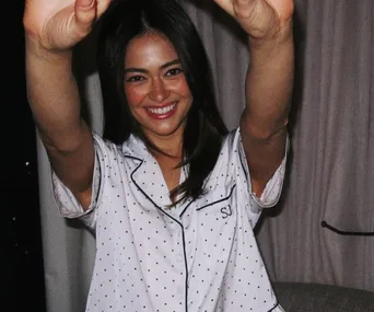 Smiling woman in polka-dot pajamas with initials "SJ" stretches arms upward in a cozy room.