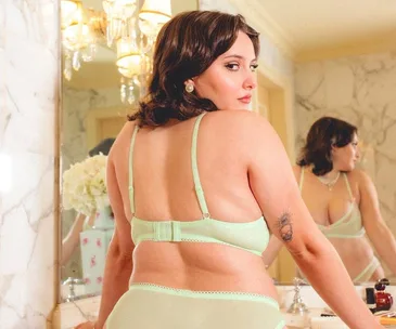 Woman in mint green lingerie looks over shoulder in elegant bathroom with marble walls and flowers in background.