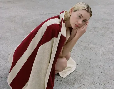 Person wrapped in a red and white towel, crouched on a concrete surface.