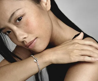 Woman wearing a silver bracelet with a heart charm on her wrist.