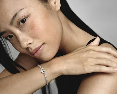 Woman wearing a silver bracelet with a heart charm on her wrist.