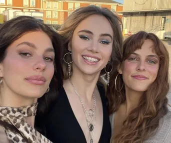 Three women smiling outdoors at a premiere event, wearing stylish outfits and hoop earrings.