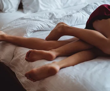 Two pairs of intertwined legs on a bed with white sheets, suggesting intimacy and relaxation.